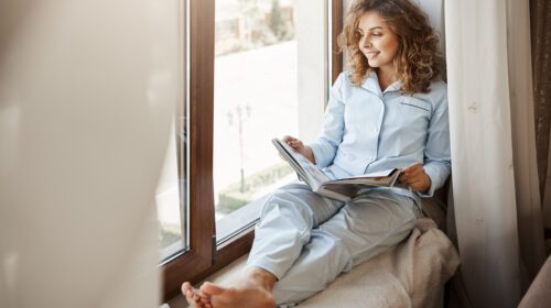 charming businesswoman having relaxing time home pleased good looking adult woman nightwear sitting window sill gazing street holding fashion magazine reading about lifestyle